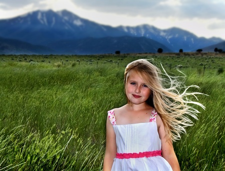 a blonde girl with wind blowing through her hair against a mountain landscapeの写真素材