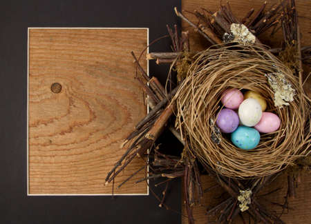 easter candy in a nest with a frame on wooden backgroundの写真素材