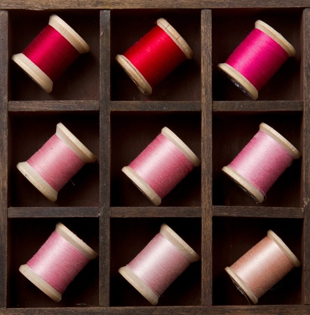 Vingtage pink and red spools of thread in a wooden printers boxの写真素材