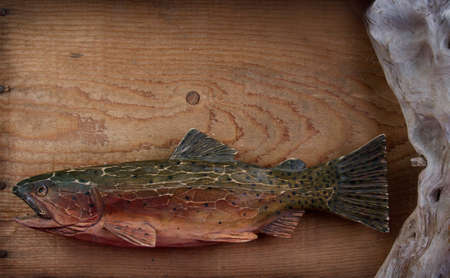 Handmade carved fish  trout  on a wooden background, with driftwood の写真素材