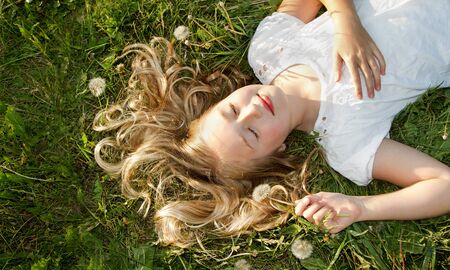 Girls sleeping in a field of grass with dandelionsの写真素材