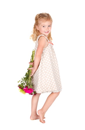 little girl holding flowers behind her back isolated on whiteの写真素材