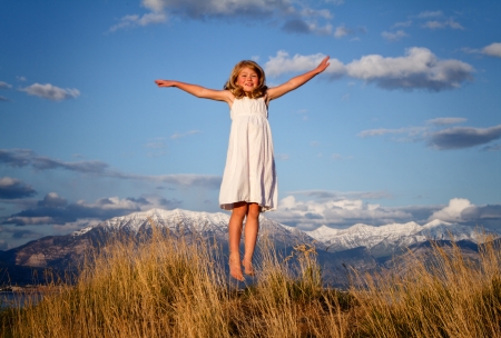 Little girl jumping in a mountain landscape with grassy foregroundの写真素材