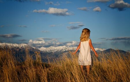 Little girl walking through tall grass in a scenic mountain landscapeの写真素材