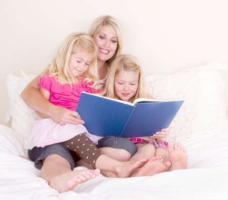 Family on bed reading book, mother and two daughters.の写真素材