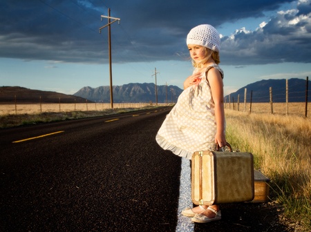 Young girl on side of road with vintage suitcases in a mountain landscapeの写真素材