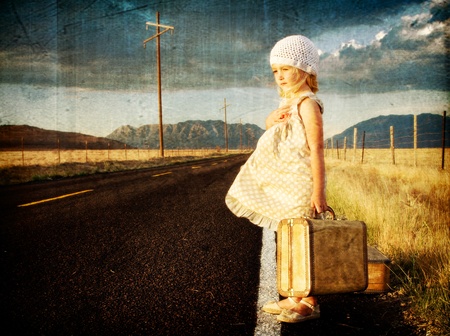 Young girl on side of road with vintage suitcases in a mountain landscapeの写真素材