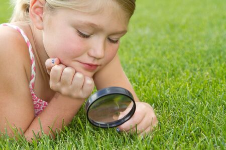 girl looking through magnifiying glass at grass outdoorsの写真素材