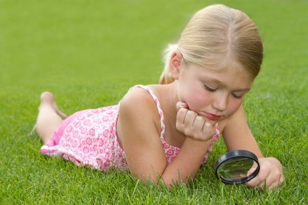 girl looking through magnifiying glass at grass outdoorsの写真素材
