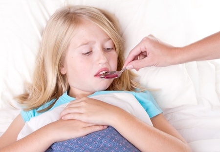 Sick girl dislikes medicine from a spoon laying in bedの写真素材