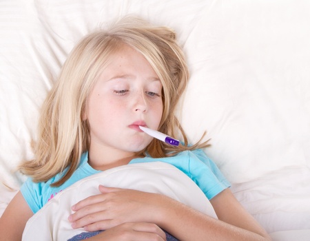 sick girl with a thermometer in mouth lying in bedの写真素材