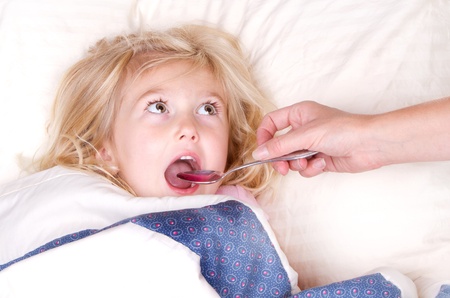 Sick child taking medicine from a spoon laying in bedの写真素材