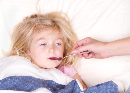 Sick child taking medicine from a spoon laying in bedの写真素材