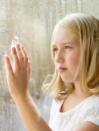 Teen or child looking out a window with rainの写真素材
