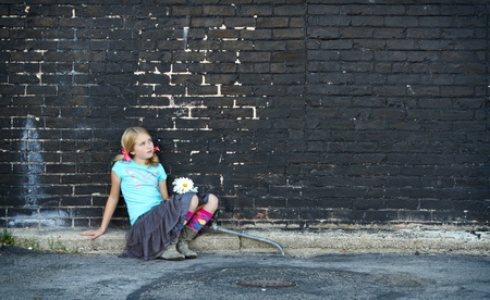 Girl sitting on ground holding flowers next to brick wallの写真素材