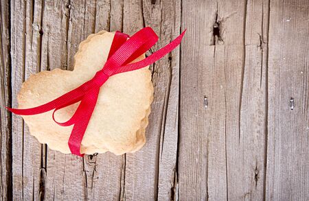 Heart shaped sugar cookie tied with red ribbon on wooden backgroundの写真素材