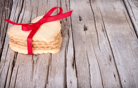 Heart shaped sugar cookie tied with red ribbon on wooden background