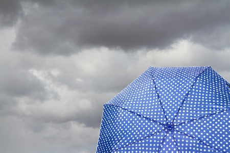 Blue polka dot umbrella on cloudy background