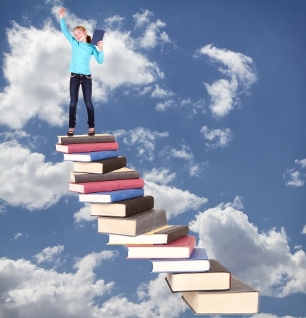 Child or girl on top of staircase of books cheering on cloudy sky backgroundの写真素材