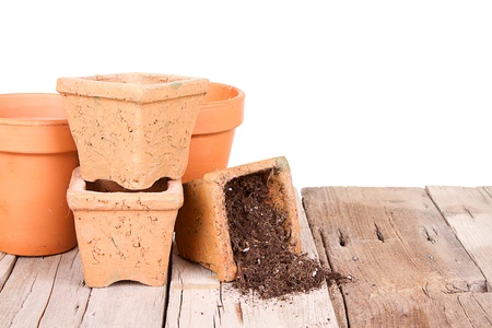 Terracotta or clay gardening pots with dirt spilling out of a pot, on a wooden plank with a backgroundの写真素材