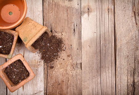 Terracotta or clay gardening pots with dirt spilling out of a pot, on a wooden backgroundの写真素材