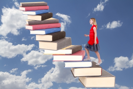 Young teen girl climbing a staircase of book with a cloudy sky backgroundの写真素材