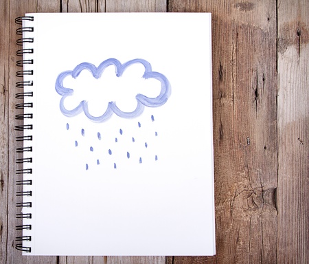 Painting of cloud and rain on notebook or sketch book with wooden planks for backgroundの写真素材