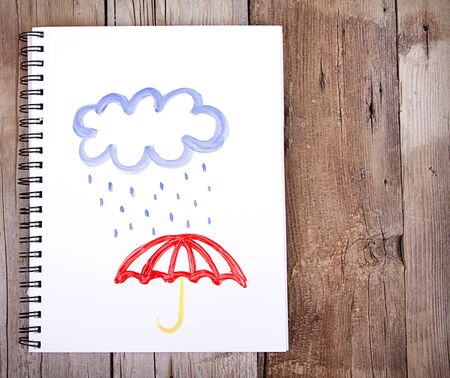 Painting of cloud and rain with umbrella on notebook or sketch book with wooden planks for backgroundの写真素材