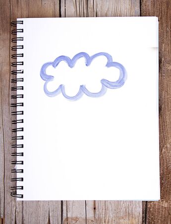 Painting of cloud on notebook or sketch book with wooden planks for backgroundの写真素材
