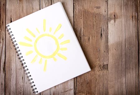 Painting of sun on notebook or sketch book with wooden planks for backgroundの写真素材