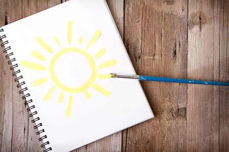 Painting of sun on notebook or sketch book with paintbrush on wooden planks for backgroundの写真素材