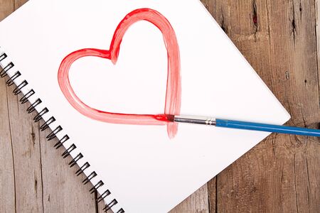 Painting of heart on notebook or sketch book with paintbrush on wooden planks for backgroundの写真素材