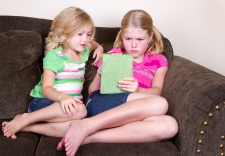 Children or sisters using a tablet while sitting on couchの写真素材