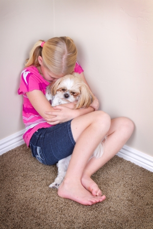 sad child in corner hugging her dog for comfortの写真素材