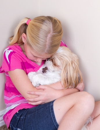 sad child in corner hugging her dog for comfortの写真素材