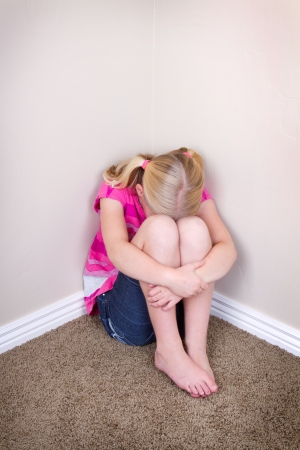child sitting alone in corner with a sad look on faceの写真素材