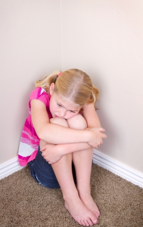 child sitting alone in corner with a sad look on faceの写真素材