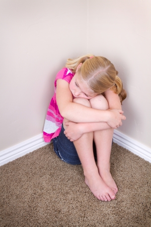child sitting alone in corner with a sad look on faceの写真素材