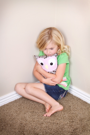 Young child or preschooler sitting in corner, with a sad look on face, holding a stuffed animal for comfortの写真素材