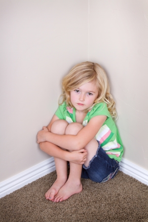Young child or preschooler sitting in corner, with a sad look on faceの写真素材