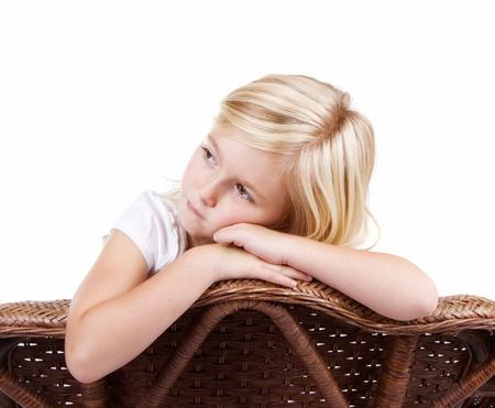 Little girl sitting in chair with a sad or lonely look on her face, isolated on white background.の写真素材