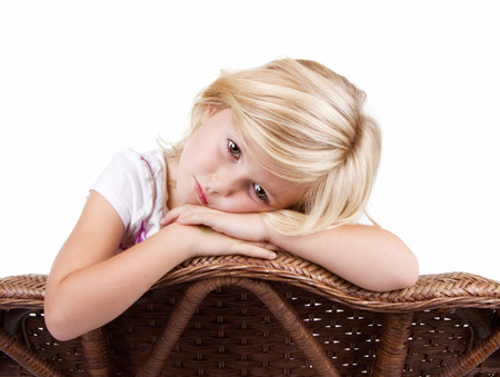 Little girl sitting in chair with a sad or lonely look on her face, isolated on white background.の写真素材