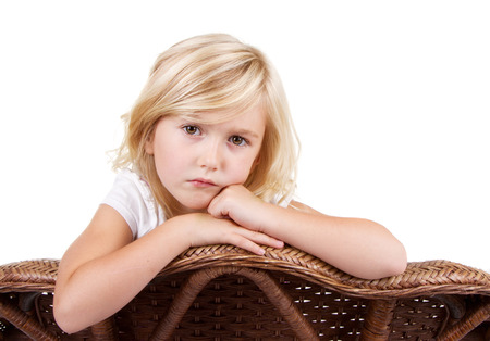 Little girl sitting in chair with a sad or lonely look on her face, isolated on white background.の写真素材
