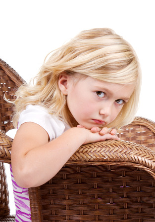 Little girl sitting in chair with a sad or lonely look on her face, isolated on white background.の写真素材