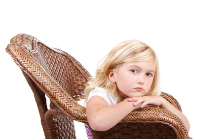Little girl sitting in chair with a sad or lonely look on her face, isolated on white background.の写真素材