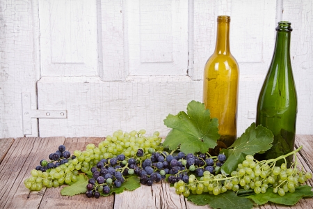 grapes on vine with leaves and empty wine bottles on wooden plankの写真素材