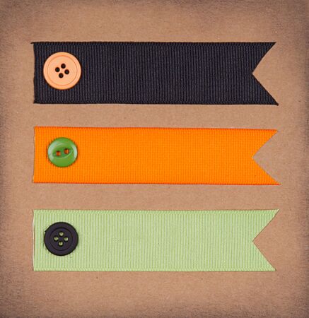 Halloween colored ribbon tags with sewing buttons on paper background for copy spaceの写真素材
