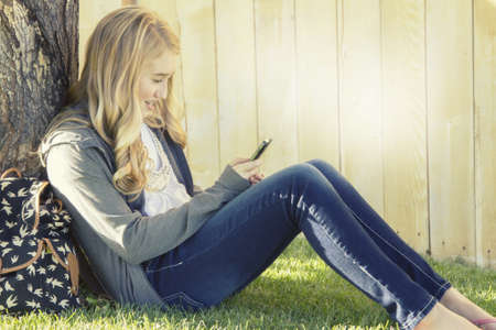 Teenage girl smiling while using a cell phone, texting, surfing the internet or playing a game, in an outdoor setting.の写真素材