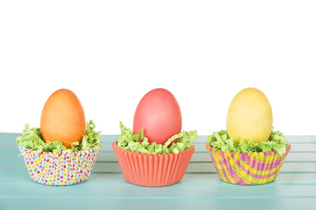 Dyed Easter eggs in a nest of green grass confetti and cup cake wrappers, on a turquoise blue wood...