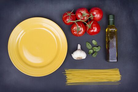 A collection of ingredients for spaghetti including pasta, tomatoes, garlic, basil and olive oil on a chalkboard backgroundの写真素材